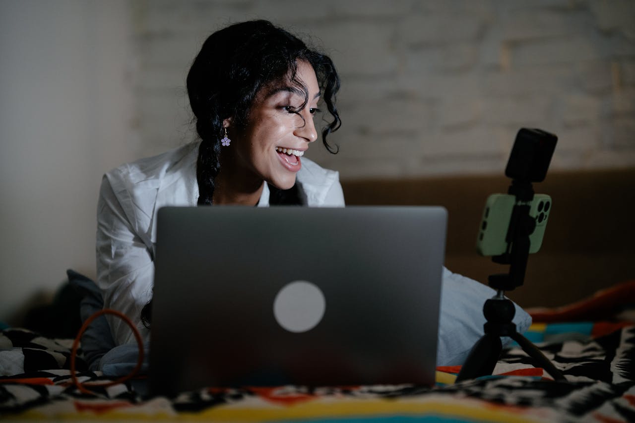 mobile-01 Happy woman vlogging with a laptop and smartphone setup, creating content indoors.